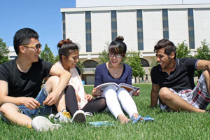 4 students sitting on the grass in the Academic Green on a sunny, blue skyed day studying 